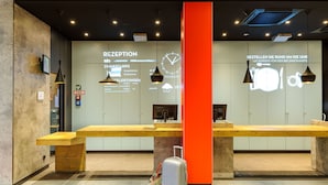 Un área de recepción con un mostrador de madera, un pilar rojo grande y una pared que muestra un reloj y opciones de menú.