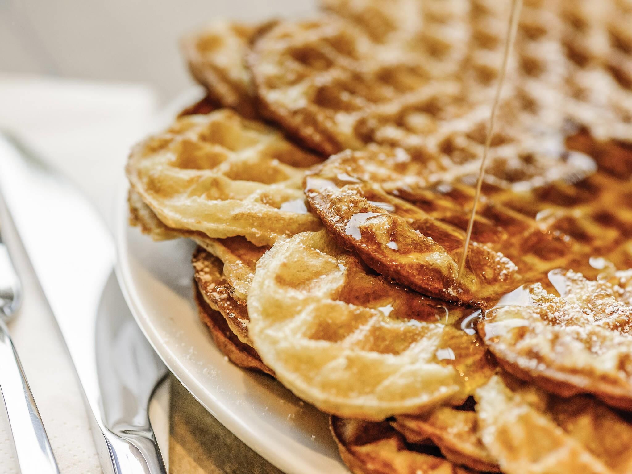 A plate of waffles with syrup being poured on them.