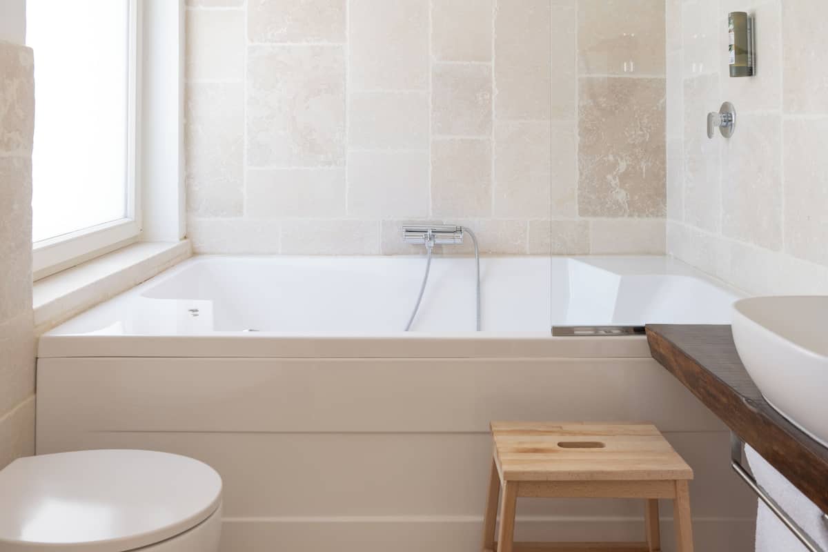 Un baño moderno con bañera, inodoro y taburete de madera.