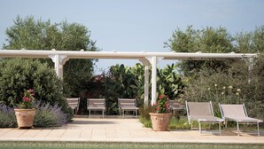 A poolside area with a pergola, lounge chairs, and potted plants. - Masseria Agrituristica Lama San Giorgio (Rutigliano)