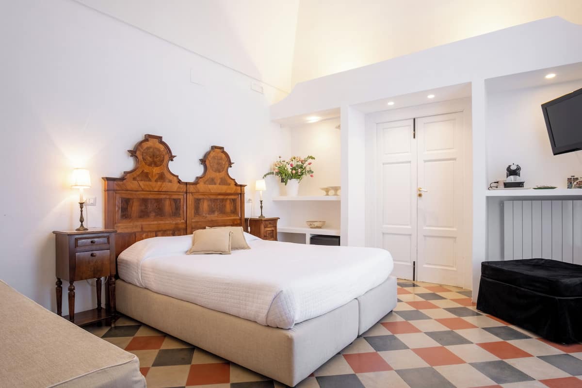 Un dormitorio con cama, mesitas de noche, cómoda, televisor y suelo estampado.