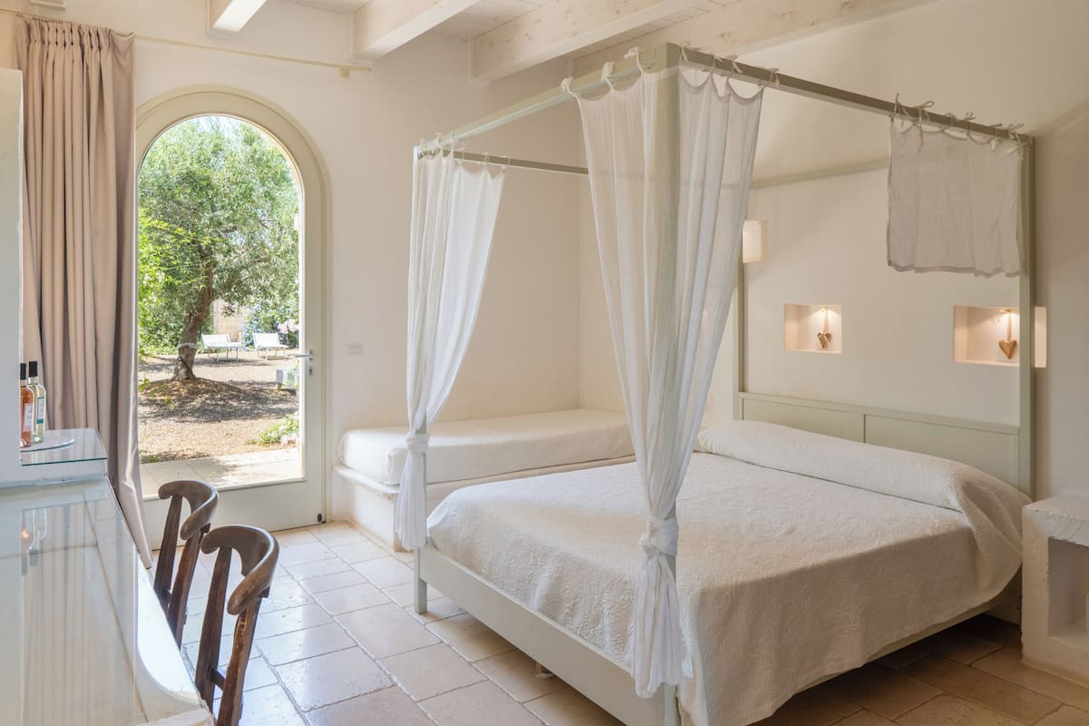 Un dormitorio con cama con dosel, una silla de madera, una mesita de noche y vistas al exterior.
