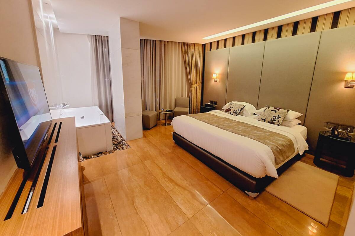 A modern hotel room with a large bed, a desk, a TV, and a sofa.