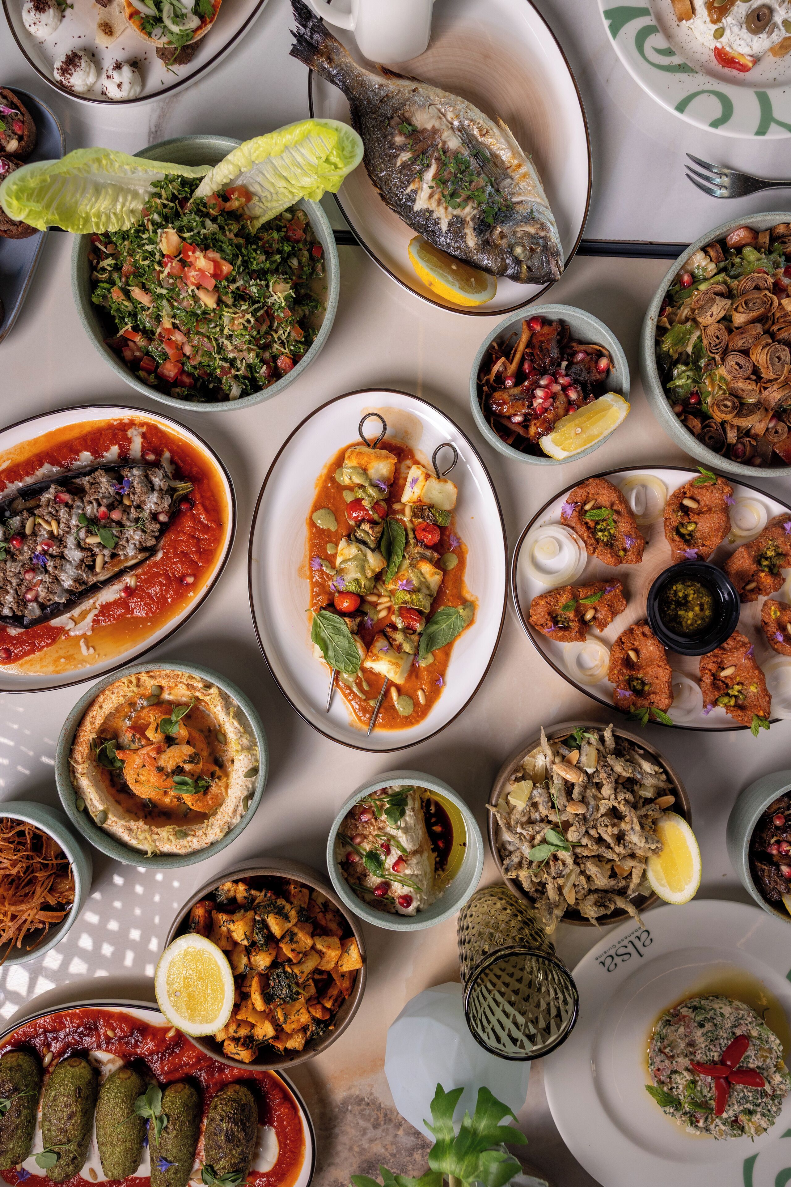 Diversos pratos sobre uma mesa, incluindo peixe, saladas e outras especialidades da culinária mediterrânea.
