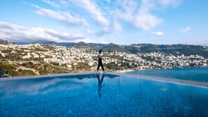 Una persona caminando sobre una terraza de piscina, con un paisaje urbano y montañas al fondo.