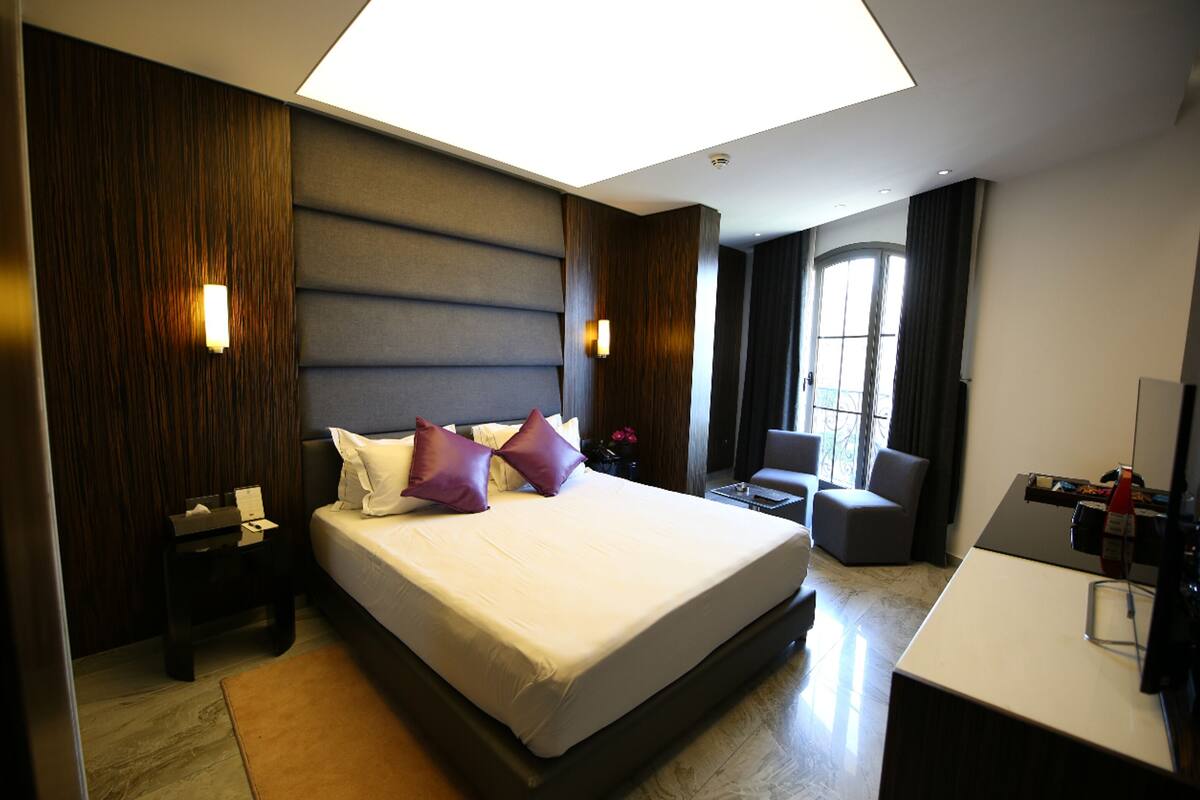 A modern hotel room with a large bed, bedside tables, a desk, and a view of the outdoors.