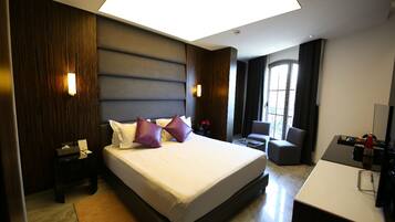 A modern hotel room with a large bed, bedside tables, a desk, and a view of the outdoors.