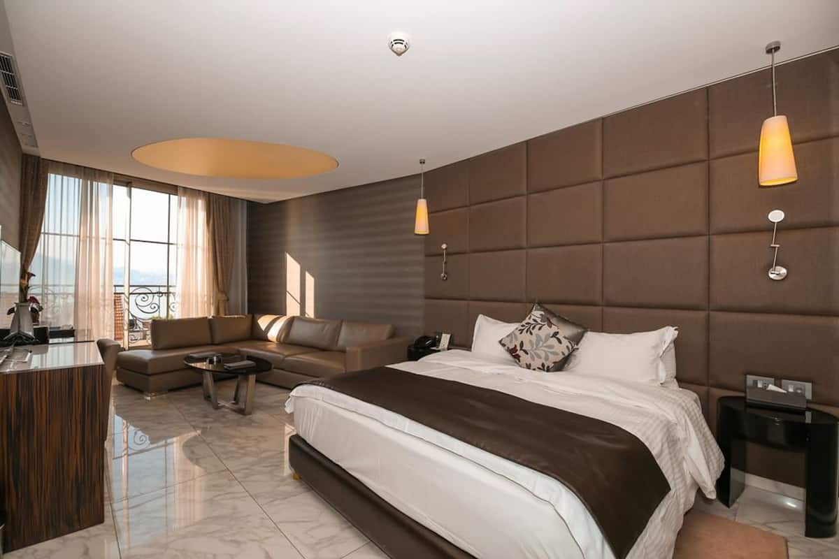 A modern hotel room with a large bed, a sofa, a desk, and a view of the city.