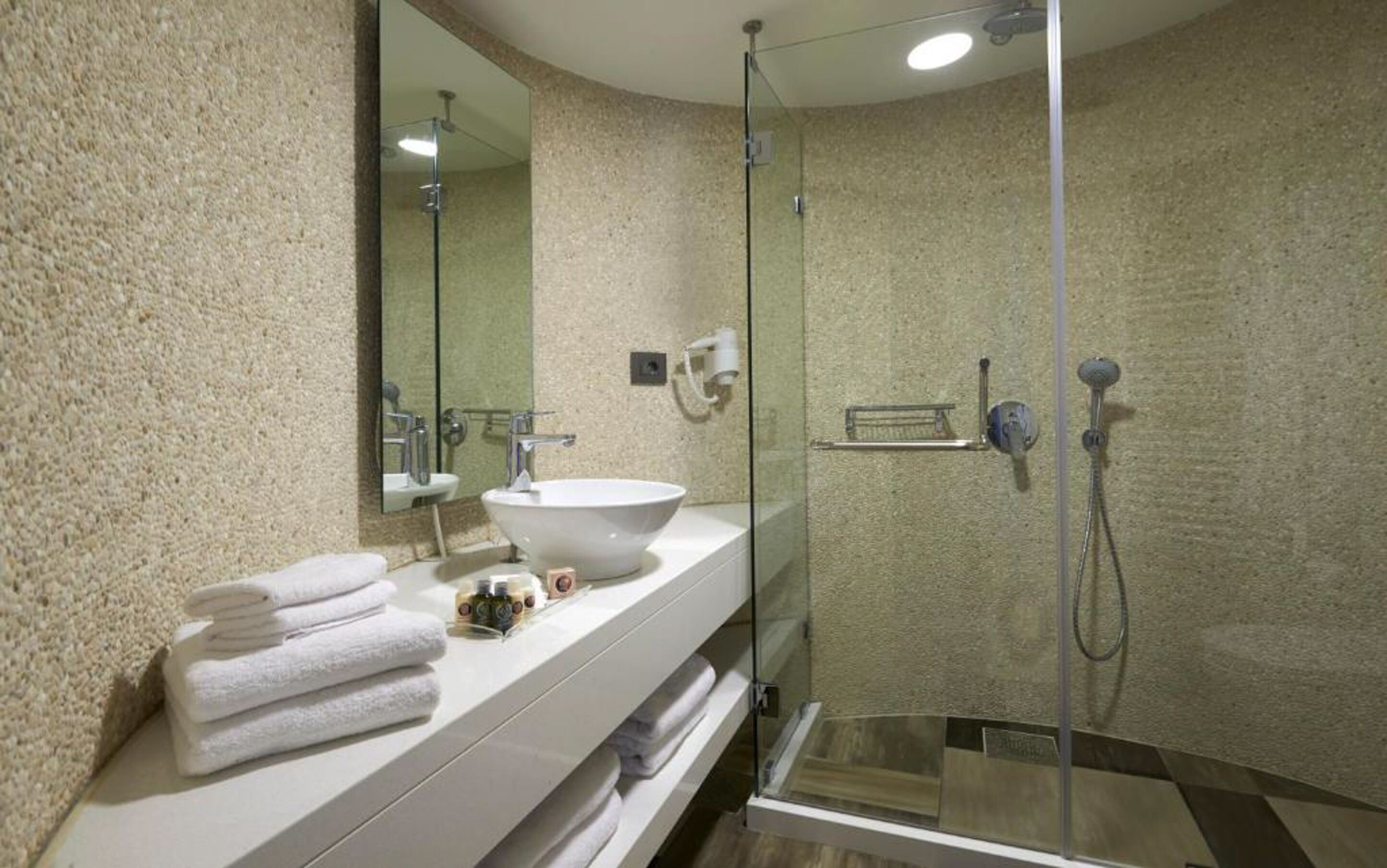 Ein modernes Badezimmer mit einer Duschkabine aus Glas, einem großzügigen Waschbecken und einem Spiegel.
