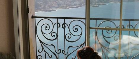 A person sitting in a bathtub with a view of a cityscape and water body through a large window.