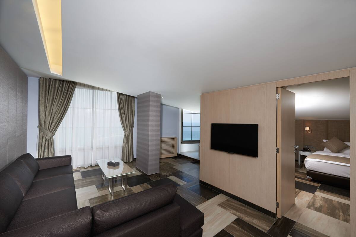 A modern hotel room with a sofa, a small table, a TV mounted on the wall, and a bed.