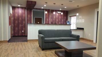 A hotel lobby with a grey sofa, a wooden coffee table, and a reception desk with a mirror.