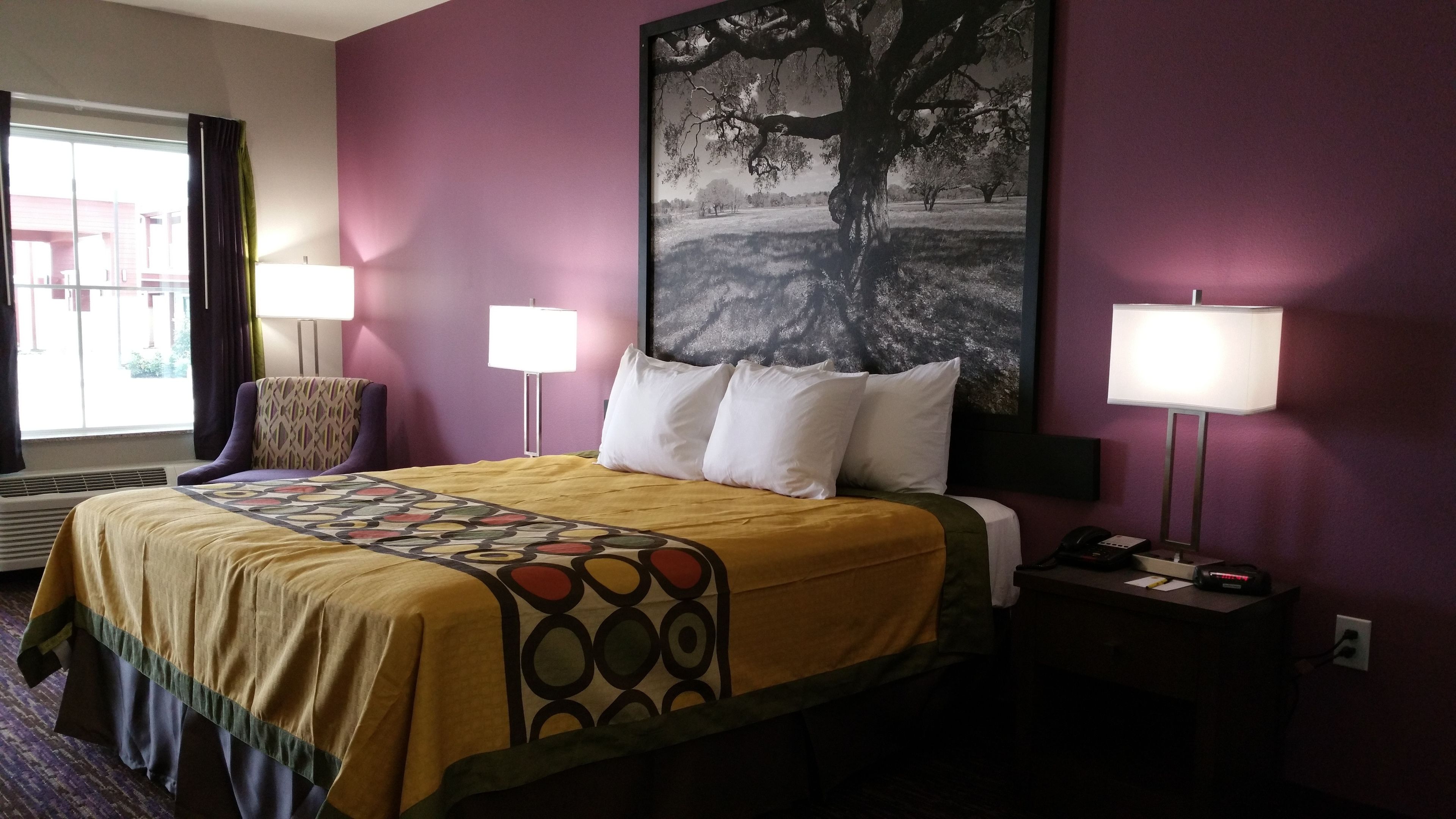 Habitación de hotel con una cama, dos lámparas de noche, una mesita de noche con un teléfono, un cuadro en la pared y una ventana con cortinas.