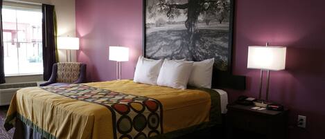 Habitación de hotel con una cama, dos lámparas de noche, una mesita de noche con un teléfono, un cuadro en la pared y una ventana con cortinas.