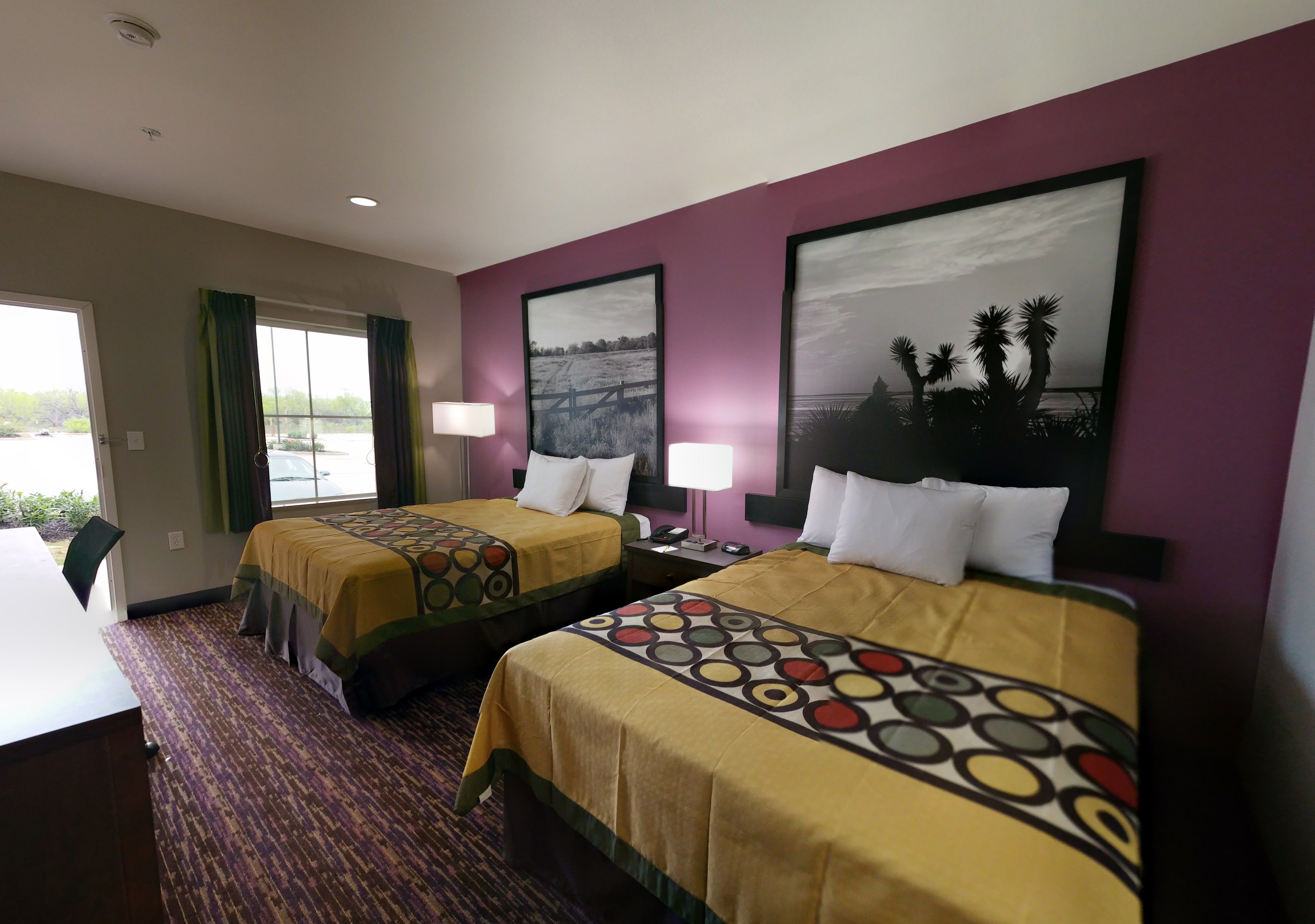 A hotel room with two beds, a desk, and a window with curtains.