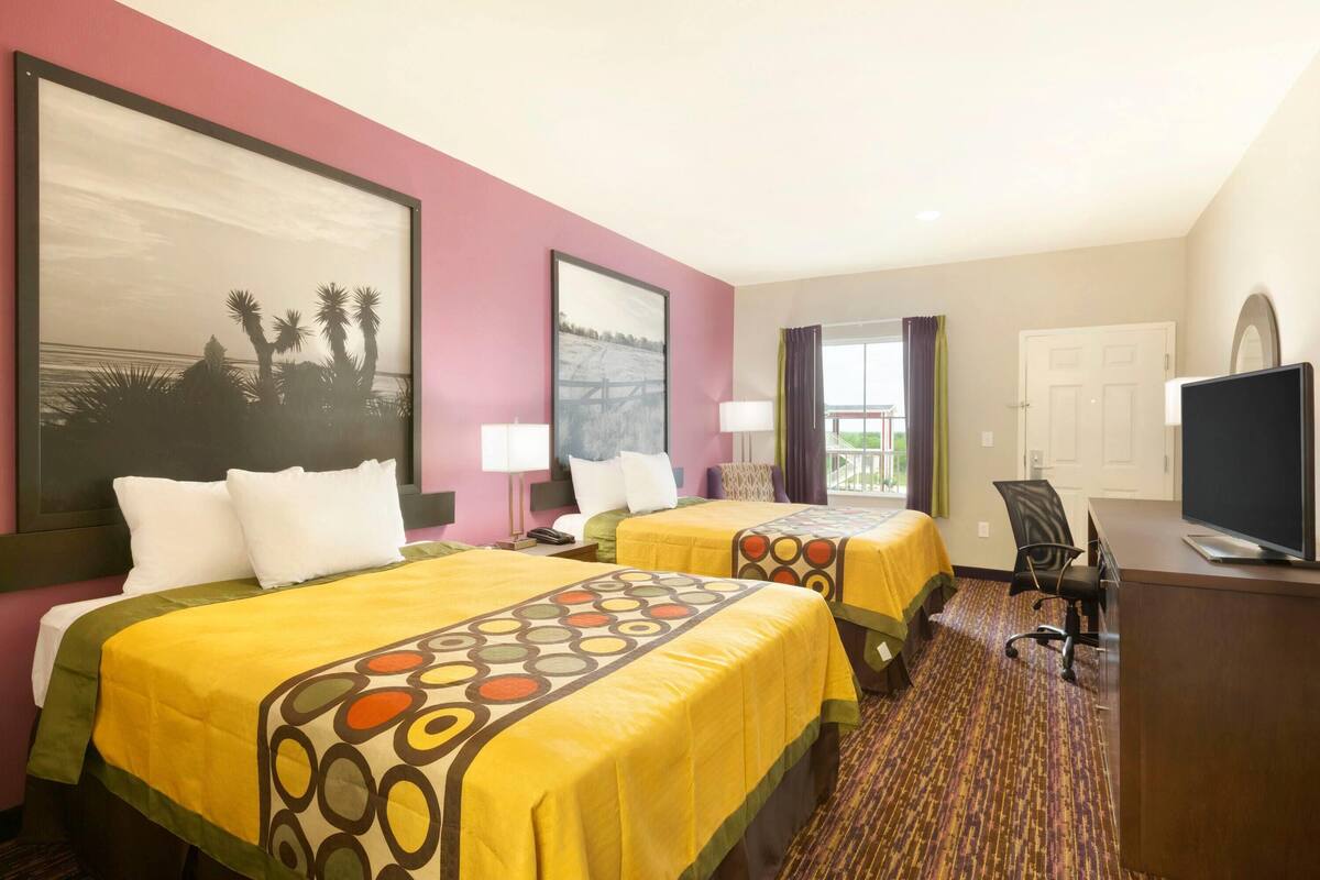 Une chambre d’hôtel avec deux lits, un bureau, une télévision et une grande fenêtre avec des rideaux.