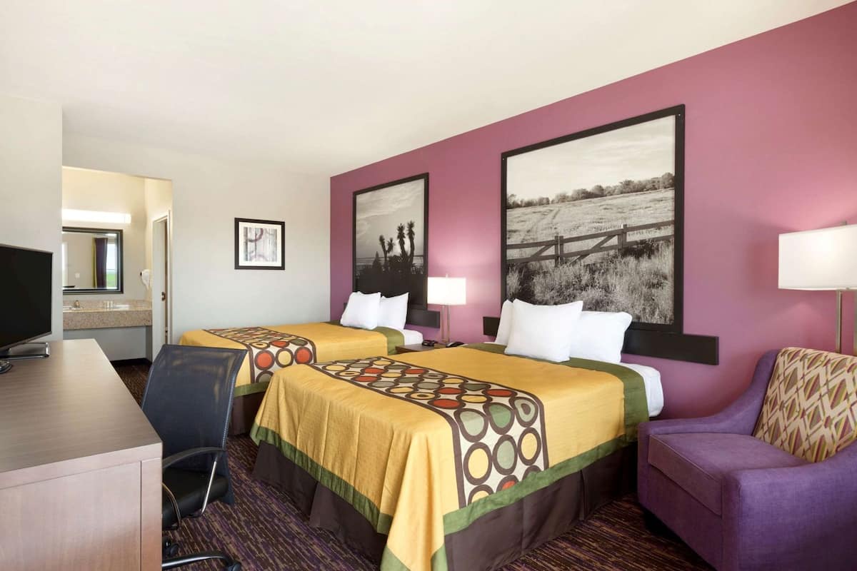 Une chambre d’hôtel avec deux lits, un bureau, une chaise, un canapé et deux lampes fixées au mur.