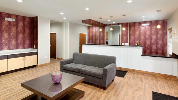Un intérieur moderne avec un canapé gris, un plancher en bois et un coin cuisine doté d’un pare-feu rouge à motifs.
