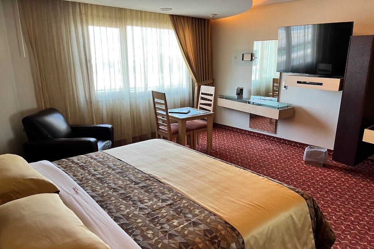 A hotel room with a large bed, a desk with a chair, a television, and a window with curtains.
