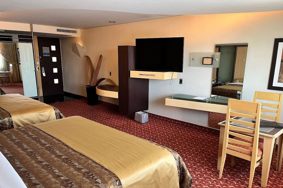 A hotel room with two beds, a desk, a chair, a television, and a minibar.