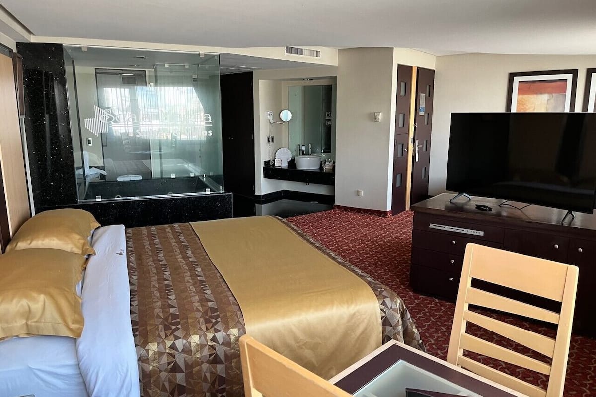 A hotel room with a bed, a desk, a chair, a television, a dresser, and a mirror.