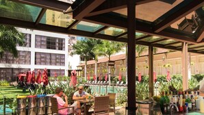Un espacio de estar al aire libre techado con mesas, sillas, piscina y sombrillas.