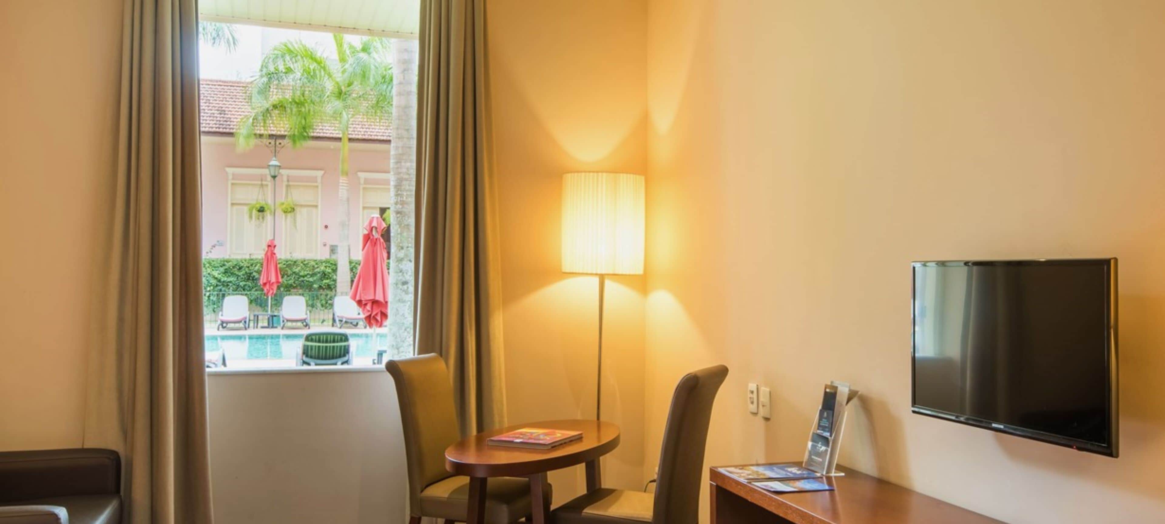 A hotel room with a pool view, a table with a lamp, and a TV on the wall.