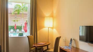 Habitación de hotel con vista a la piscina, una mesa con lámpara y televisor en la pared.