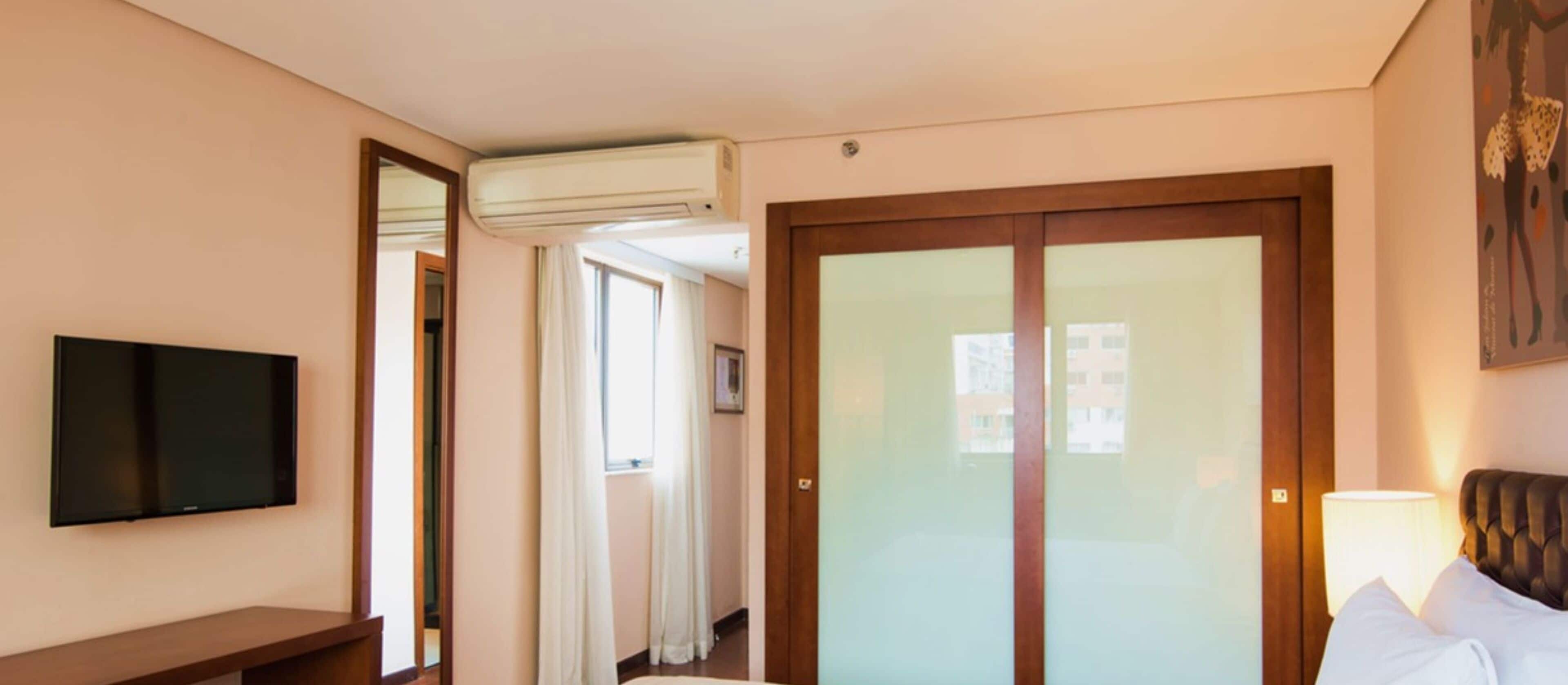 Ett hotellrum med en platt-TV, en säng med sänggavel, ett nattduksbord och ett fönster med gardiner.