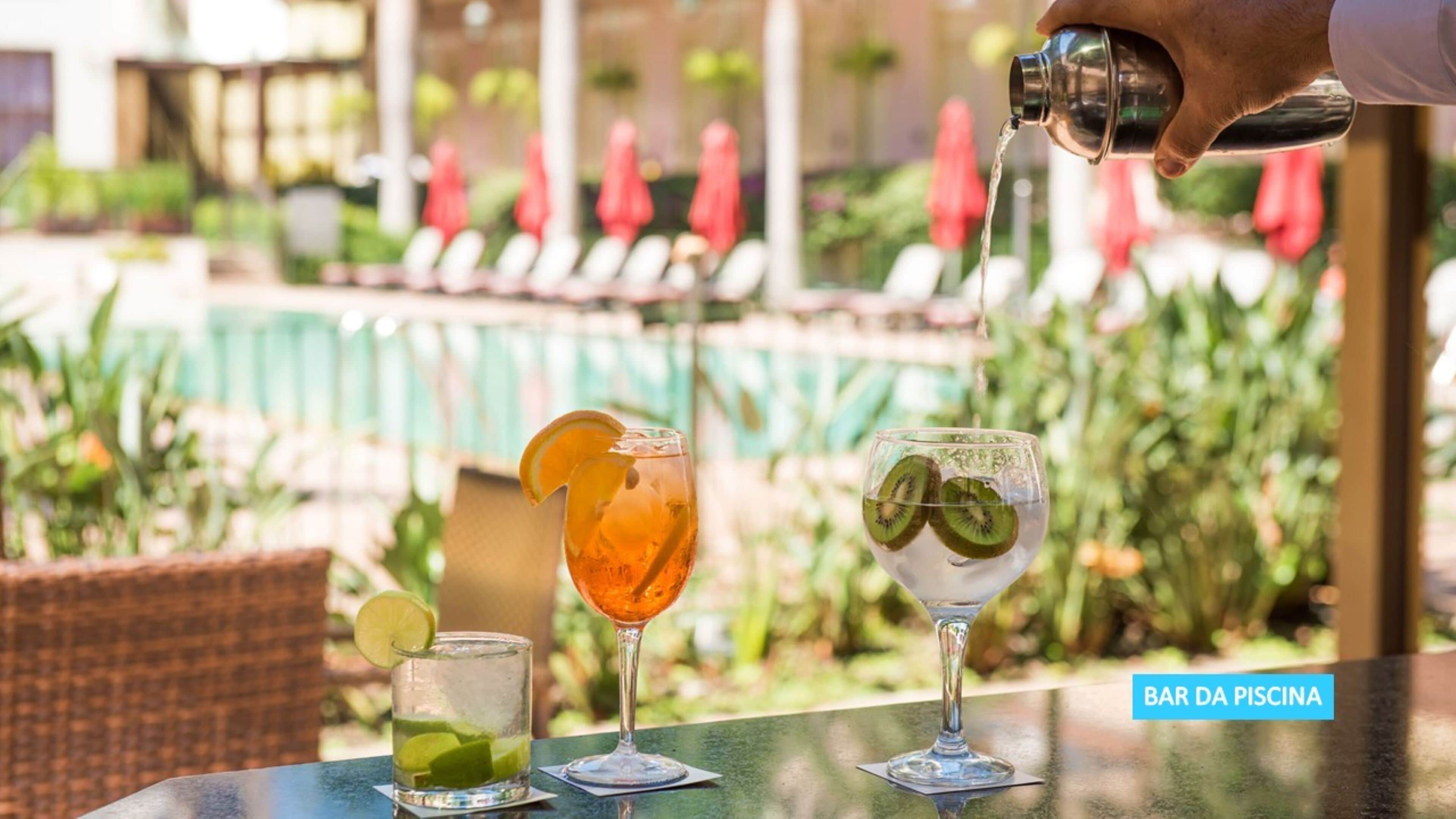 A bar area with a pool view, featuring three drinks on a table.