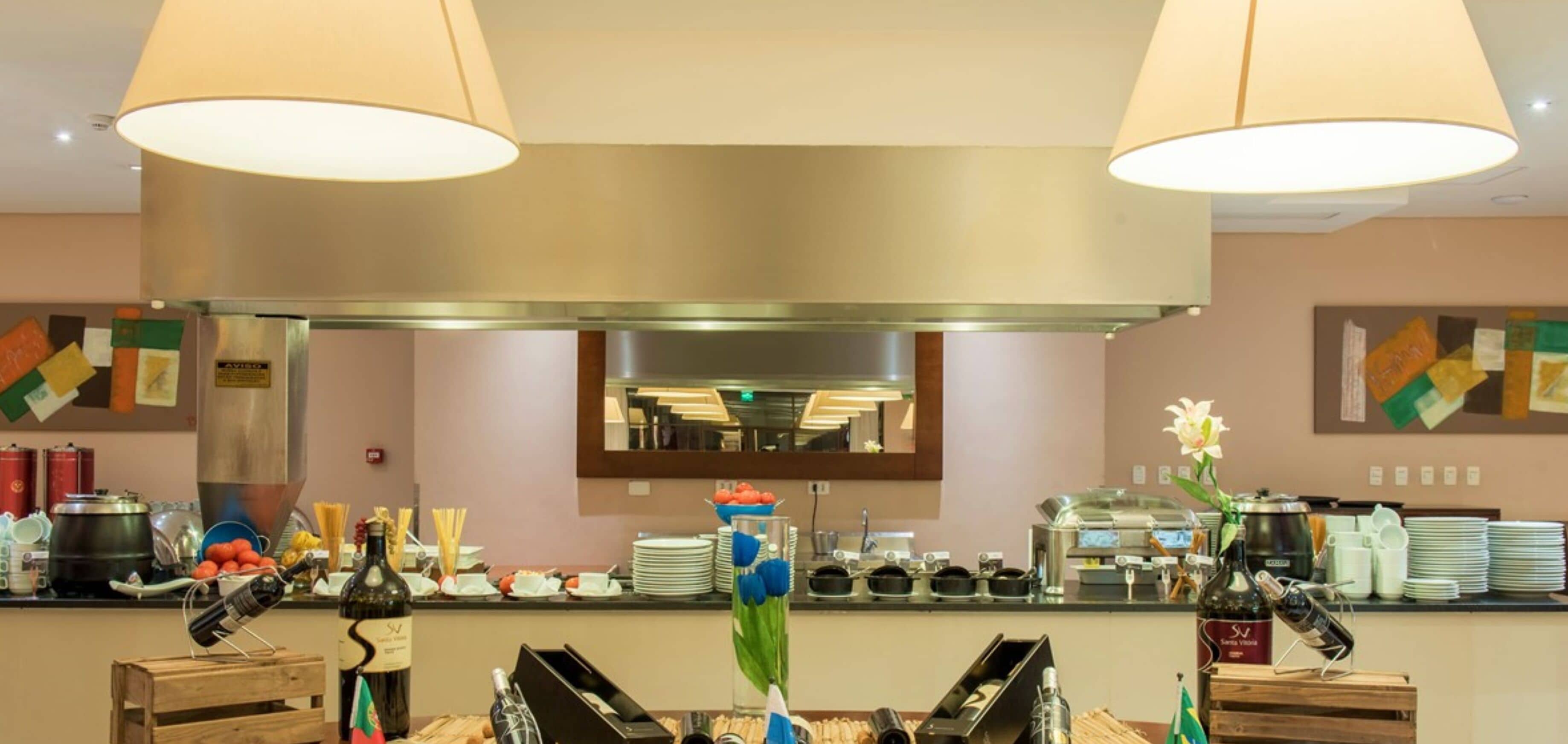 Una cocina de hotel con una campana extractora de acero inoxidable, un espejo grande sobre la encimera, y diversos utensilios y electrodomésticos.
