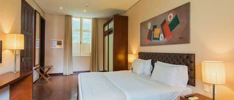 Habitación de hotel con una cama grande, un escritorio, una silla, una ventana y un cuadro en la pared.
