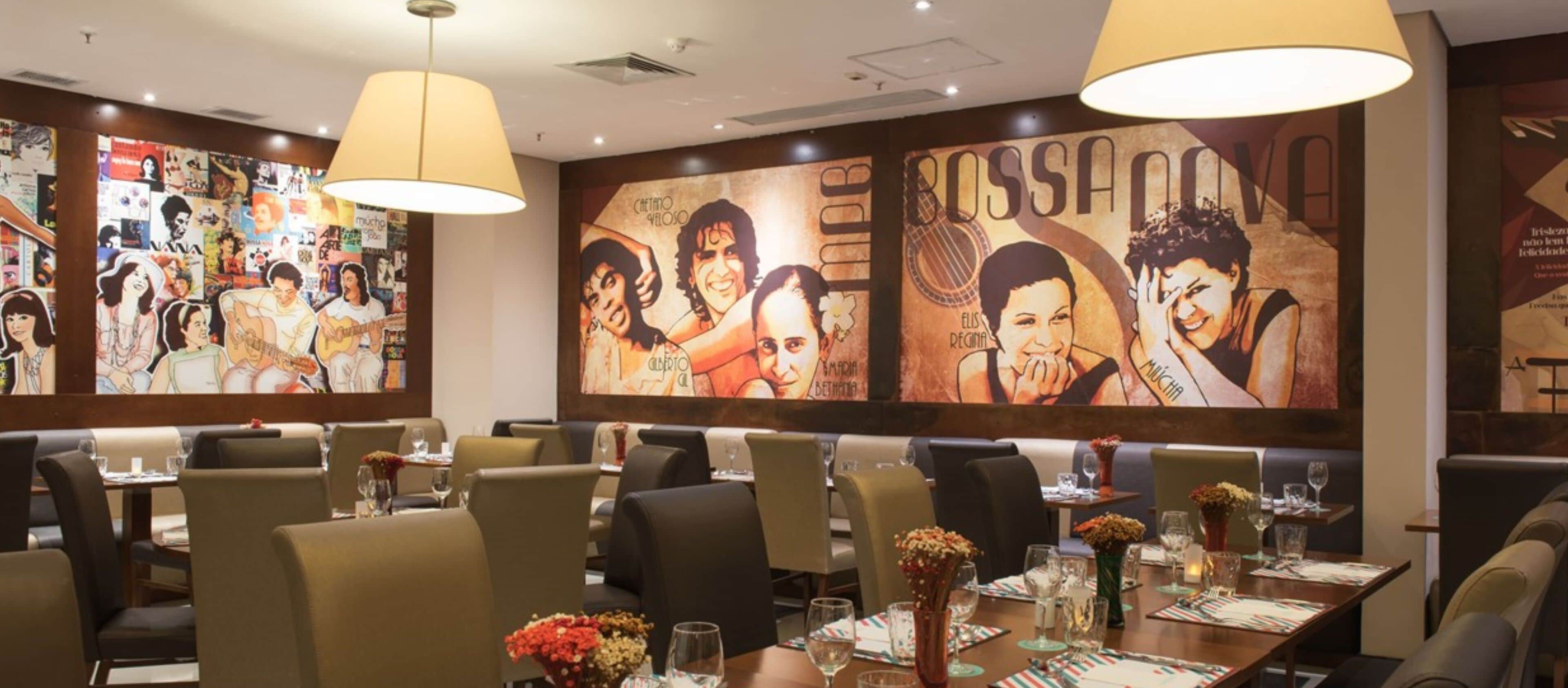Um restaurante com cabines, mesas dispostas com copos e talheres, e obras de arte nas paredes.