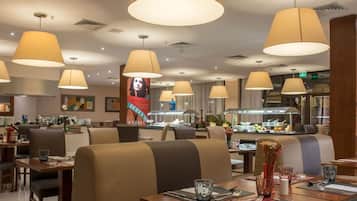 Restaurante moderno com mesas altas, assentos confortáveis e iluminação pendente.