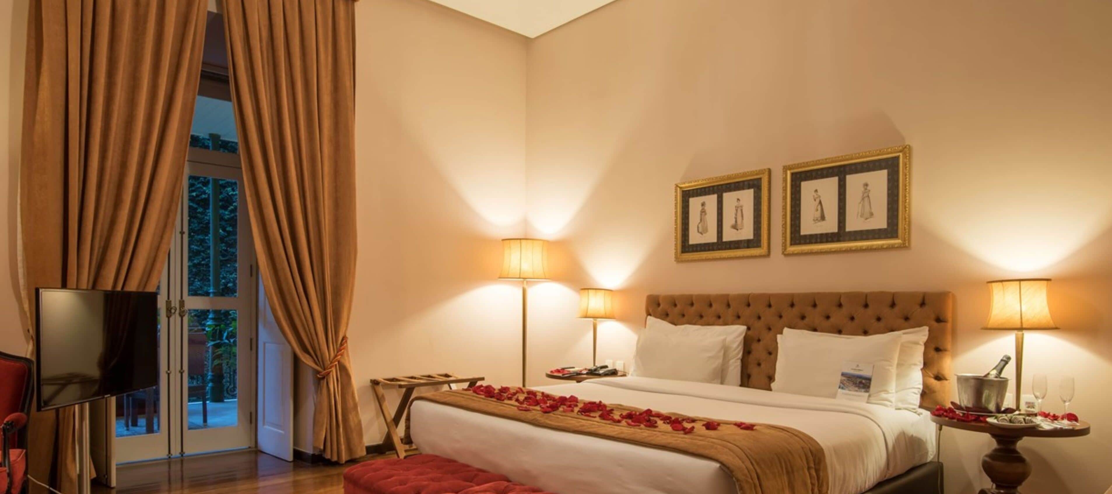 A hotel room with a large bed, two bedside lamps, a flat-screen TV, and a large window with curtains.