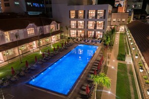 A swimming pool with lounge chairs and umbrellas, surrounded by a well-lit building with multiple windows. - Vila Galé Rio de Janeiro (Rio de Janeiro)