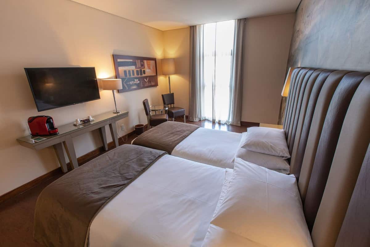 A hotel room with two beds, a desk with a coffee maker, a TV, and a chair.