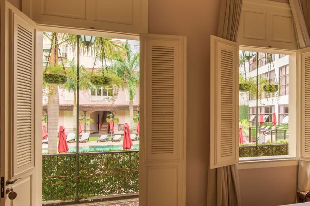 A hotel room with a bed, a nightstand, a lamp, and a view of an outdoor pool area with lounge chairs and umbrellas.
