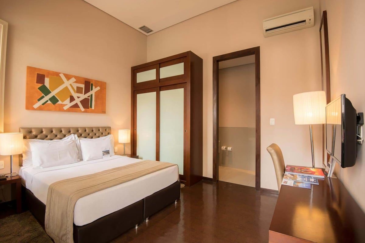 Habitación de hotel con cama, escritorio con silla, televisor y puerta con paneles de vidrio esmerilado.
