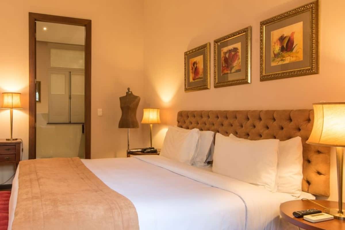 A hotel room with a large bed, two bedside lamps, a red chair, a desk, and a wardrobe.
