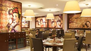 A restaurant with multiple dining tables and chairs, large hanging lamps, and a wall with various posters and artwork.