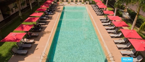 Una piscina rectangular con sillas de descanso y sombrillas rojas a ambos lados.