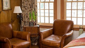 A room with two brown leather armchairs, a wooden side table with a lamp, a potted plant, and a window with a view of a snowy landscape. - The Old Inn On The Green (Great Barrington)