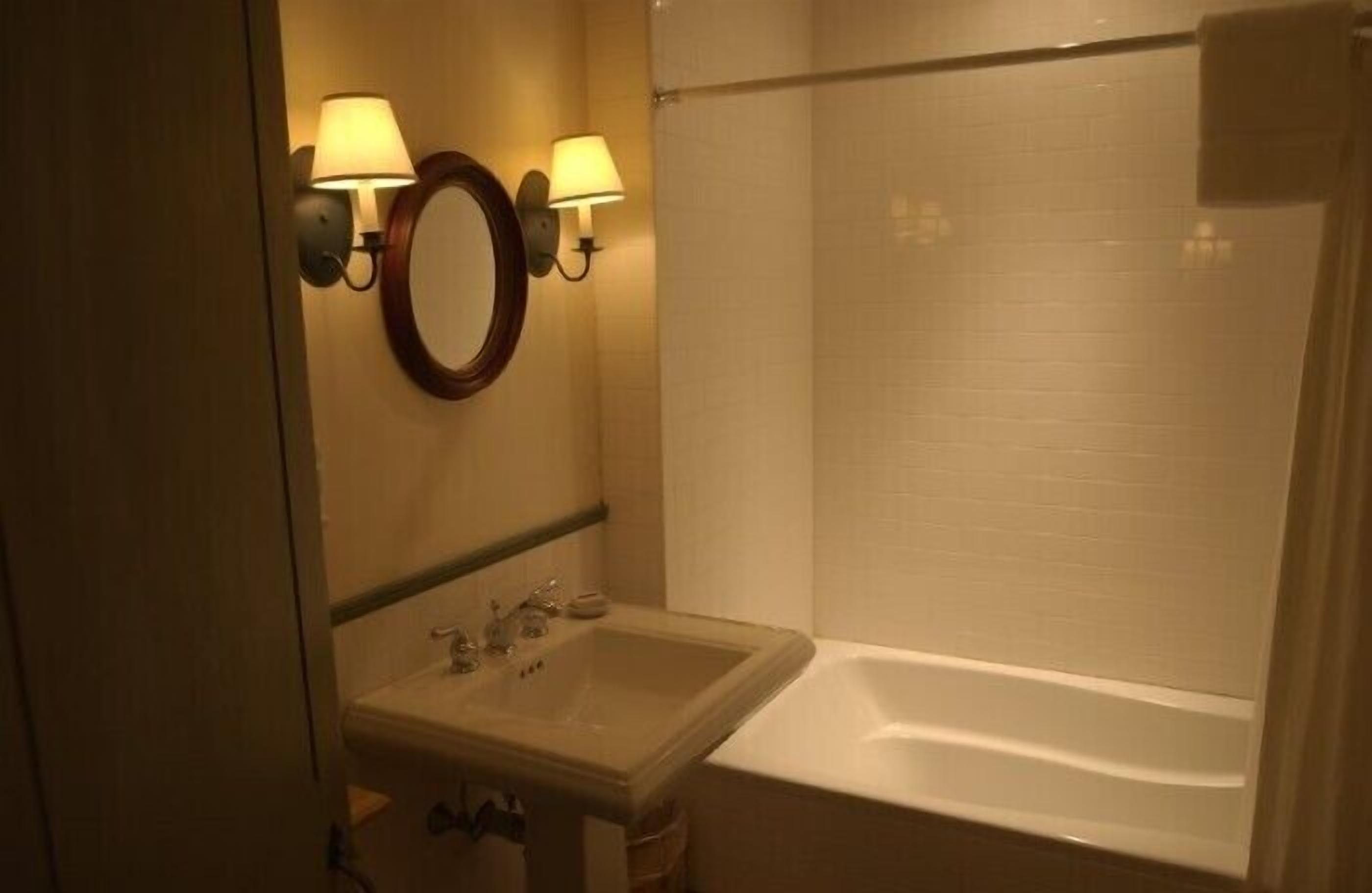A bathroom with a sink, mirror, two wall-mounted lights, and a shower.