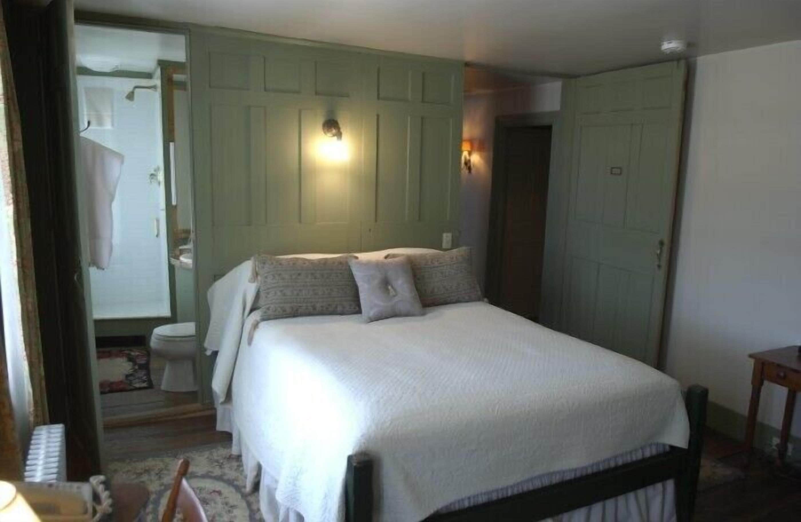 A bedroom with a bed, a nightstand, a dresser, and a mirror. There is a door leading to a bathroom.