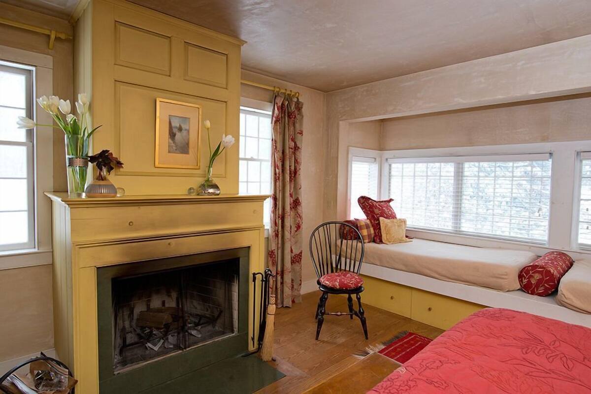 A cozy room with a fireplace, a bench with cushions, and a window with a view.