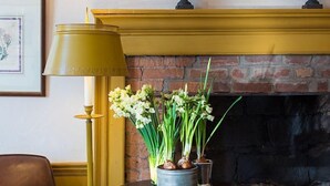 A room with a leather armchair, a table with a potted plant, a lamp, and a fireplace with decorative elements. - The Old Inn On The Green (Great Barrington)