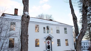 A white two-story house with a front door, windows, and a chimney. - The Old Inn On The Green (Great Barrington)