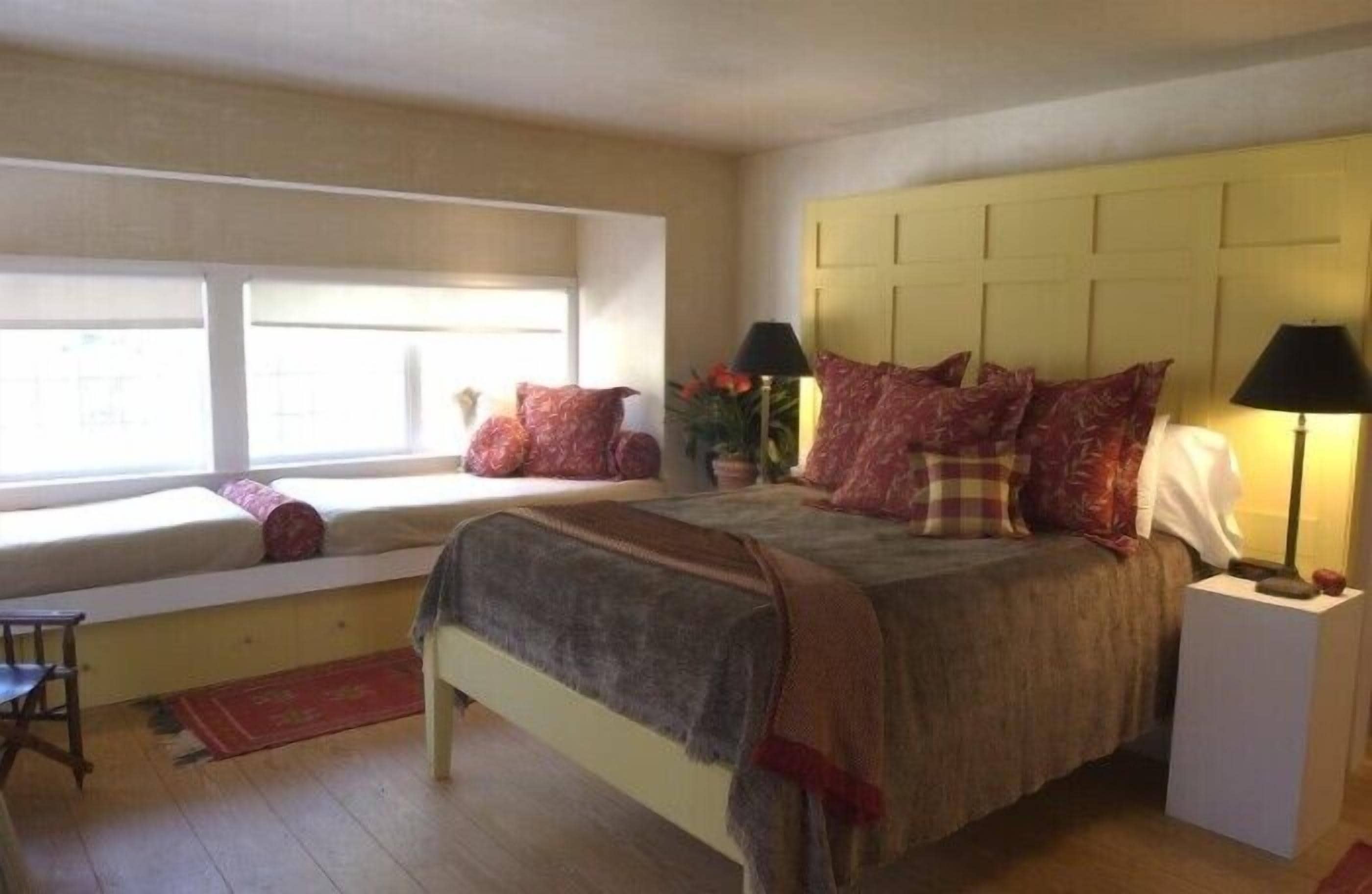 A bedroom with a bed, bedside lamps, a window seat, and a small table.