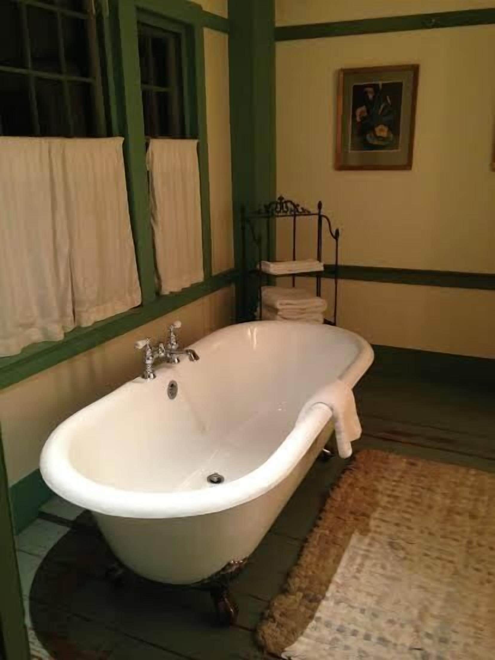 A bathroom with a freestanding bathtub, a window with curtains, and a framed picture on the wall.
